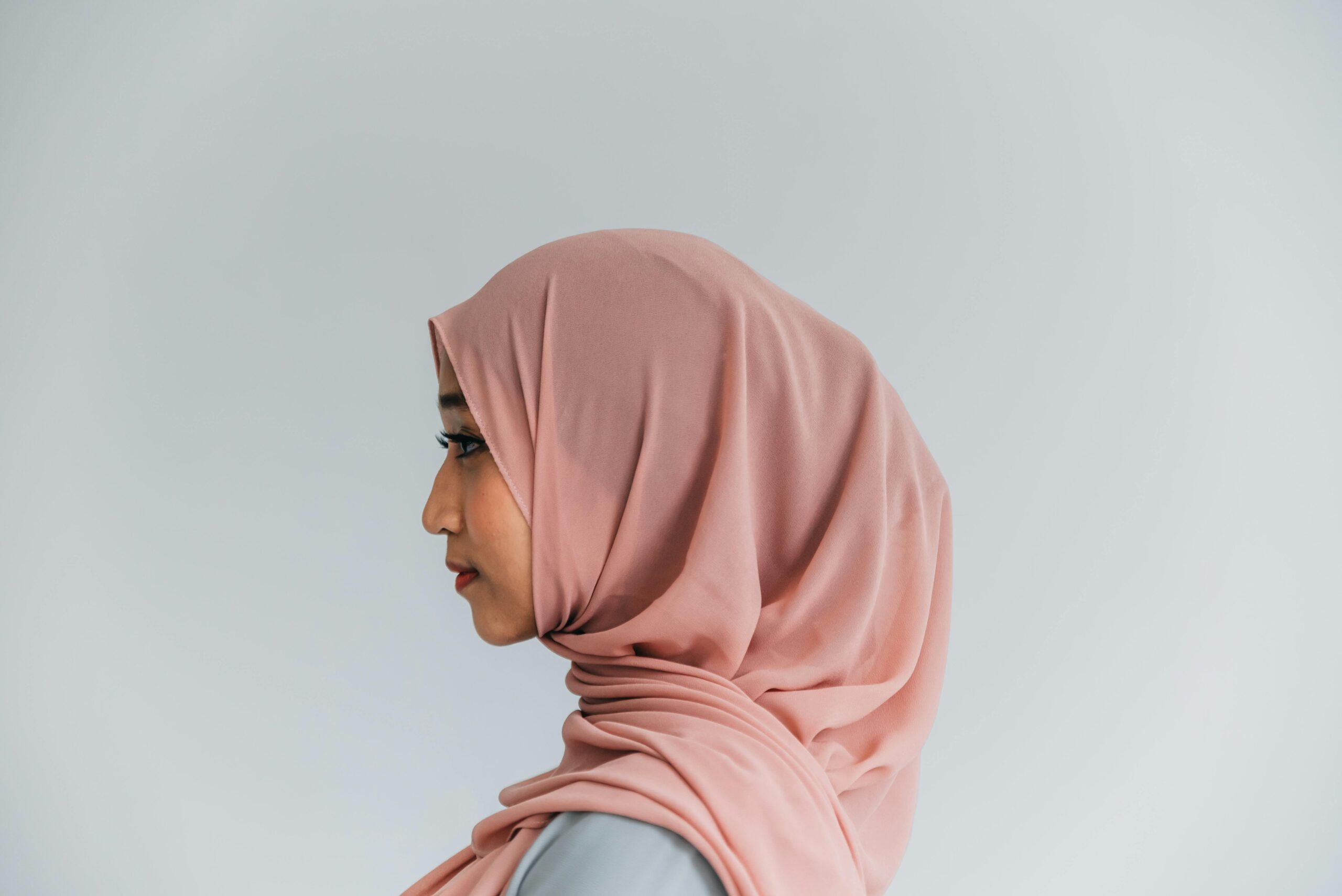 Elegant side view portrait of a woman wearing a hijab, set against a soft plain background.